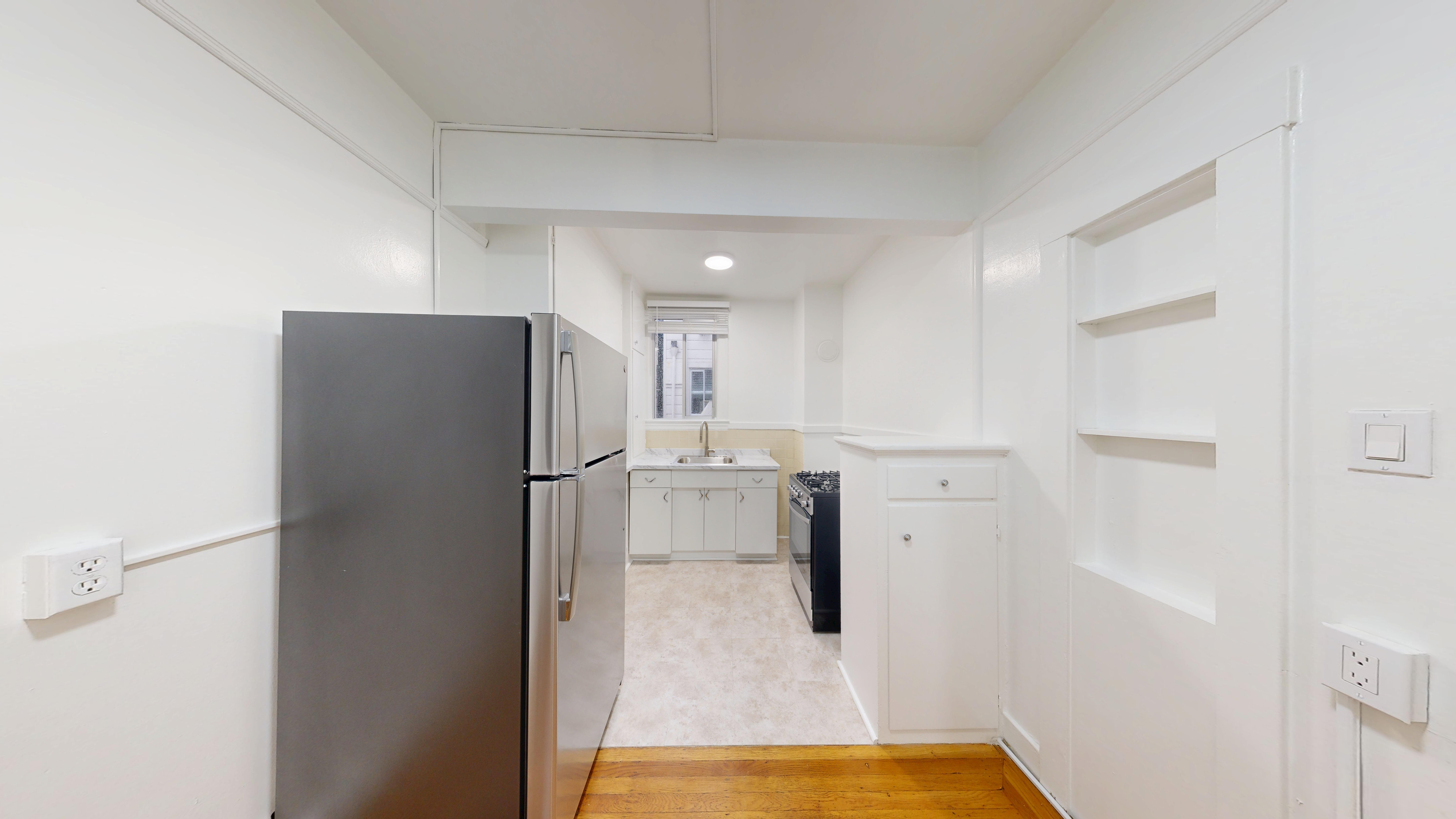 A kitchen with a black fridge and white walls.